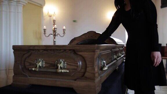 悲伤的女人在葬礼上将红玫瑰放进棺材