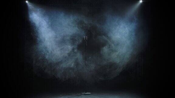 一个老式的金属麦克风隐现在烟雾弥漫的黑色演播室背景中烟雾消散麦克风在演播室的灯光下闪闪发光