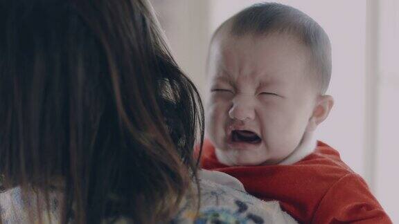 在慢镜头中一位亚洲母亲抱着一个女婴试图安抚和安慰她在家里哭泣的婴儿