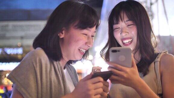 两个亚洲女性朋友在晚上使用智能手机