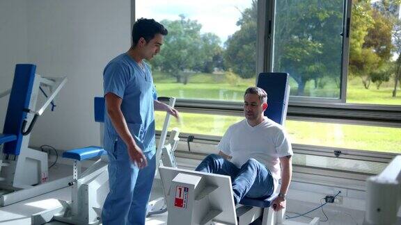 男治疗师指导他的病人在物理康复中心的机器上锻炼他的腿