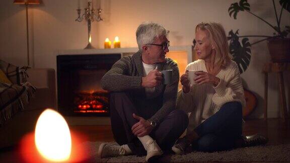 快乐的老夫妇一起在壁炉边放松在家里喝咖啡