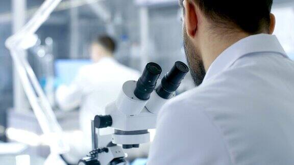 从一个研究科学家的肩膀看显微镜他和他的同事在现代实验室进行实验