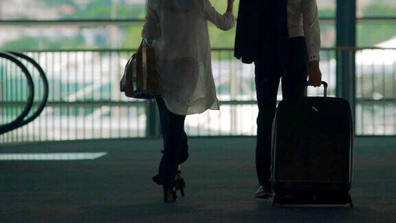 已婚夫妇走过机场天桥男人提着行李箱度假