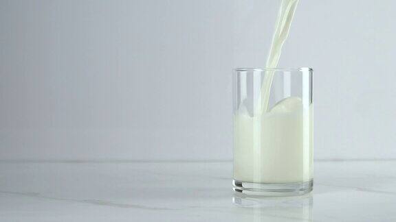 慢镜头:将牛奶倒入白色背景的玻璃杯中