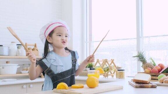 可爱的小女孩戴着厨师帽拿着木沙拉勺在厨房里欢快地跳舞