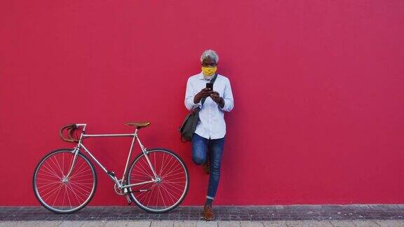 非裔美国老年人戴口罩骑自行车用智能手机站在p