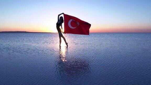 美丽的芭蕾舞演员在水上举着一面土耳其国旗有风的一天