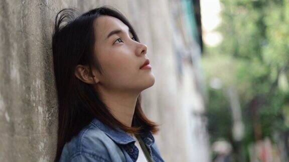 美丽年轻的亚洲女性孤独的感觉倚在墙上在泰国曼谷的一个小街道