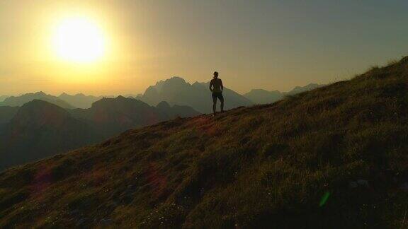 航拍:日落时分年轻女子爬上山顶的剪影
