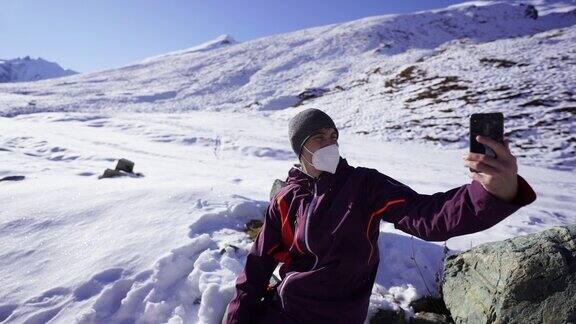 滑雪者戴着健康面具在雪山中使用手机进行视频通话