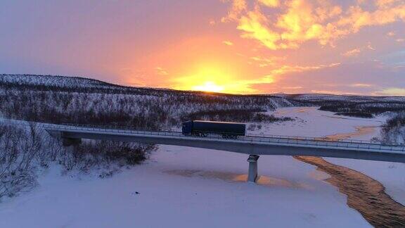 冬季日落时分半挂车穿过结冰的河流上的桥