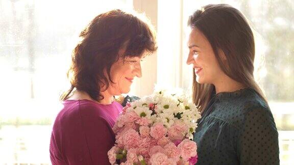年轻的成年女子女儿拥抱快乐的中年母亲拥抱亲情用母亲节祝贺成熟的母亲献上鲜花一起庆祝