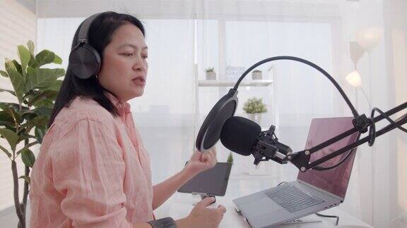 亚洲女性电台主持人录制播客在她的笔记本电脑与耳机和麦克风女播客制作音频播客从她的家庭工作室的在线节目