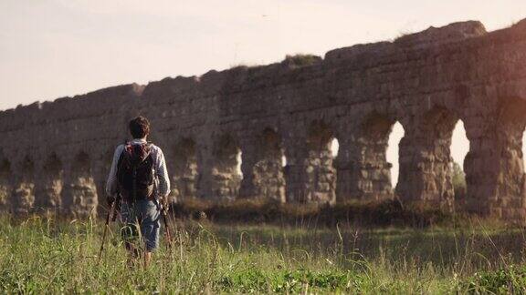 年轻的背包客光着脚走在罗马高架渠拱门前的草地上在日落慢镜头parcodegliacquedotti公园废墟