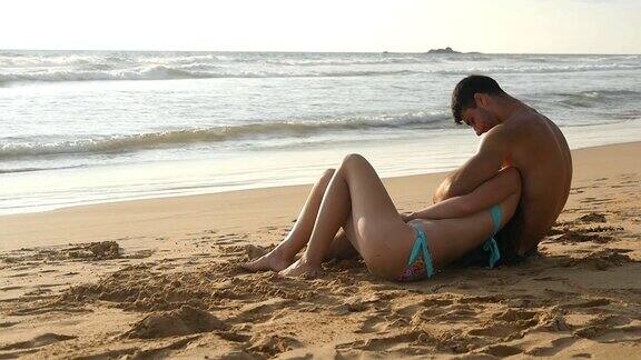 一对年轻浪漫的情侣坐在沙滩上拥抱着欣赏美丽的风景一个女人和一个男人一起坐在海边的沙滩上欣赏着大海和风景慢动作特写