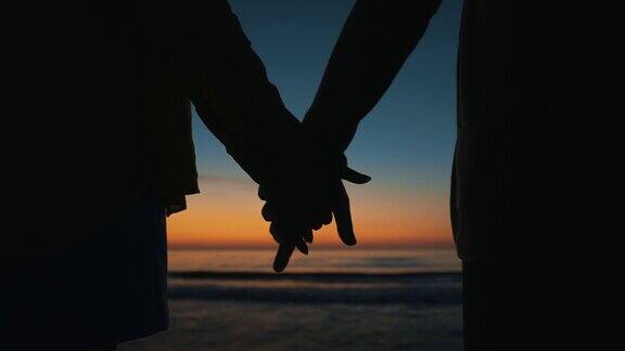 夕阳西下相爱的情侣在海边手牵着手