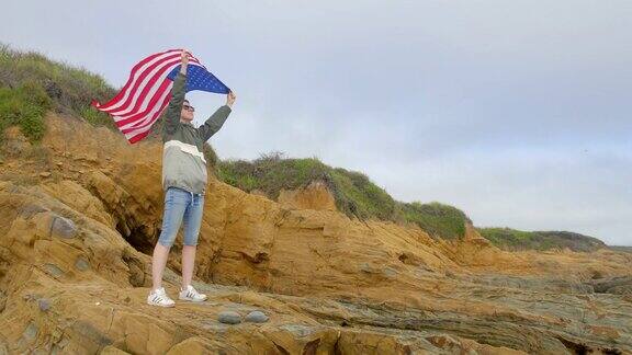 在太平洋狂野海岸的岩石上举着美国国旗的女人加州