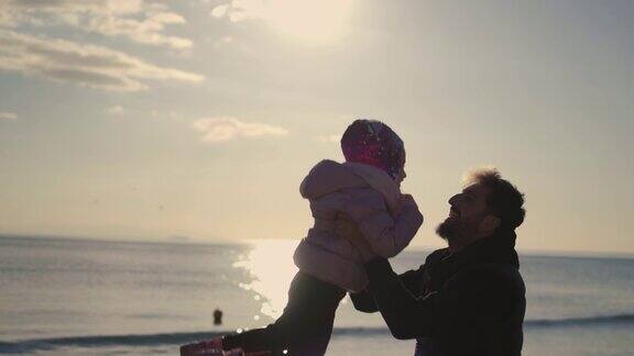 父亲把女儿抛向空中超级慢动作冬天的一天父亲把女儿抛向沙滩上的空中