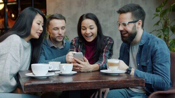 快乐的女孩和男孩使用智能手机触摸屏在咖啡馆聊天和大笑