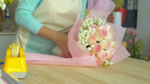 花店花店老板用包装纸把玫瑰花束包起来