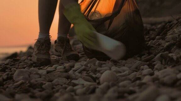 生态一名戴着橡胶手套的志愿者清理岸边的垃圾脚的特写背景是日落环境保护