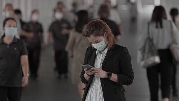 商业女性戴着医用口罩站在人群中使用智能手机慢镜头