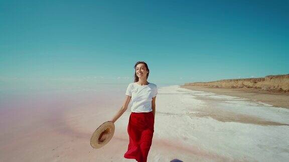 优雅美丽的女人旅行者快乐在明亮的粉红色的湖盐平底鞋女孩穿着长红色裙子和拿在手里的帽子