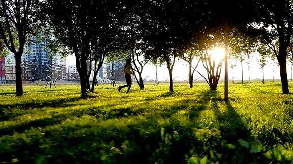 日落时分女孩在城市公园里奔跑慢镜头光线穿过树林摄像机在移动