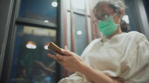 年长的亚洲妇女在晚上使用智能手机时会戴口罩
