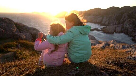 两个小女孩坐在北部海滩的海岸岩石上欣赏日落或黎明