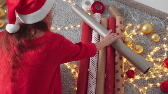 年轻女子正在为她的朋友和亲戚包装圣诞礼物戴圣诞帽的女孩用红色包装纸制作新年包裹装饰为冬季假期做准备