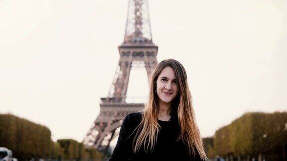 年轻快乐的女子站在法国巴黎埃菲尔铁塔附近对着镜头微笑并发送飞吻