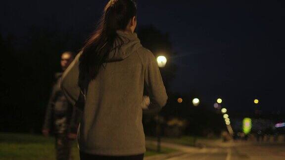 晚上在城里慢跑一个年轻的女运动员在路灯下沿着堤岸慢跑后视图