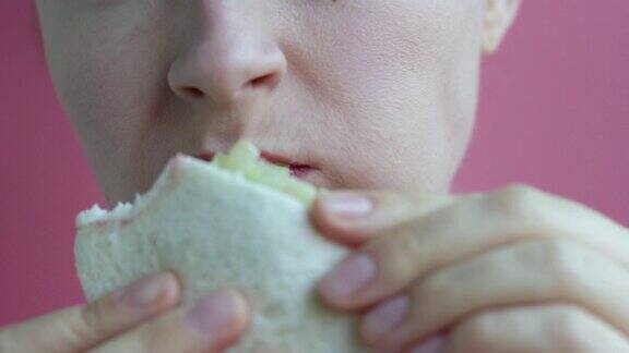年轻女子吃三明治的特写在粉红色的背景