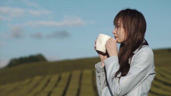 一个迷人的女人站在茶园里用白色的大杯子喝茶