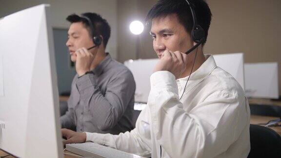 侧视图亚洲男性呼叫中心代理提供专业的客户服务在他的工作站