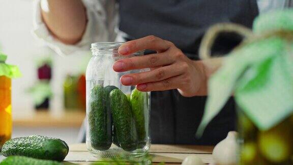 大蒜活跃的女人堆叠在一个玻璃罐子里准备黄瓜保存在厨房里