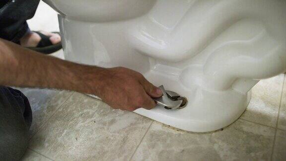 一个白人修理工取下螺栓盖用一个活动扳手松开将卫生间与地板连接的螺母