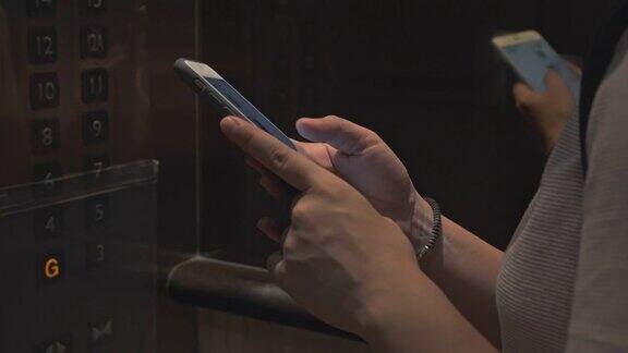 一名妇女戴着防护口罩在电梯里使用智能手机