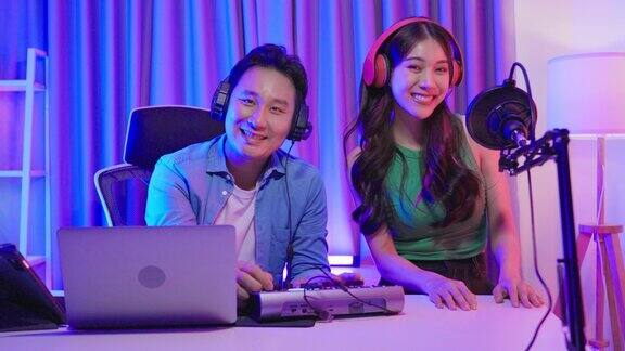 亚洲音频DJ男和女看着镜头在播音室年轻漂亮的女性和男性博客网红戴着耳机在演播室为电台录制早间新闻播客节目