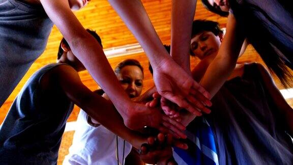 体育老师和学校学生在篮球场上形成手堆