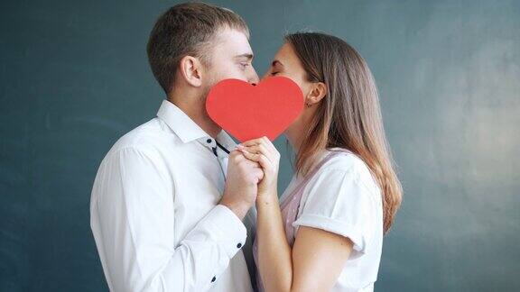 在灰色的背景下美丽的年轻夫妇在情人节卡片后面接吻