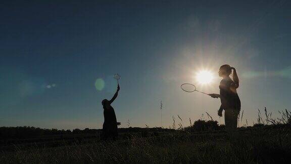 母亲和女儿在日落的背景下打羽毛球