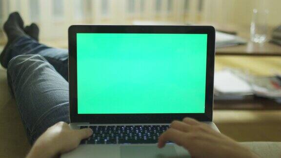 躺在家里的沙发上使用绿色屏幕的笔记本电脑
