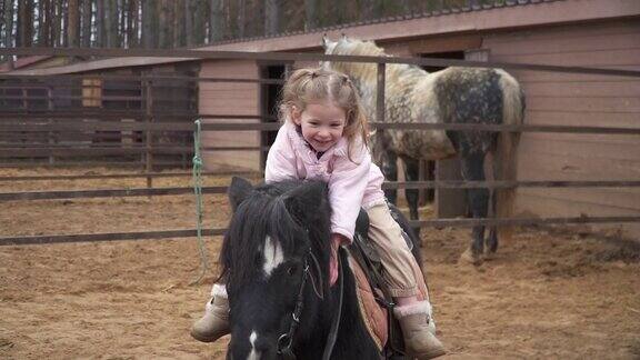 快乐的孩子坐在小马上农场里的骑手马拥抱她的宠物女孩笑着说