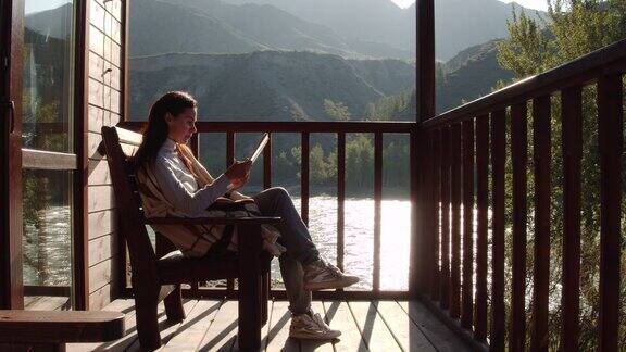 一名年轻女子在乡村别墅阳台上舒适的扶手椅上看书