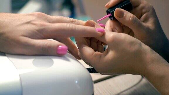 特写美甲大师:在女人的手上涂上粉色指甲油
