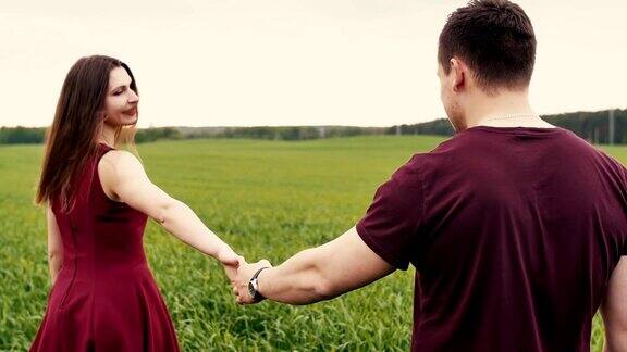 浪漫的年轻情侣在爱牵手走在一片长草的田野慢动作稳定器拍摄