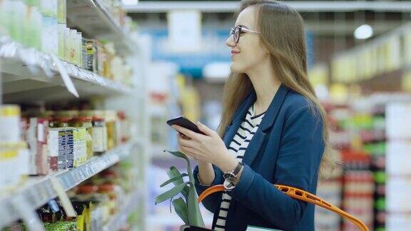 在超市:美丽的年轻女子在浏览商店的罐头食品区时使用智能手机她检查她的购物清单并拿